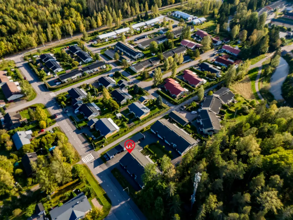 Korkea ilmakuva asuinalueesta, metsästä ja joesta, kohde merkitty sijaintimerkillä